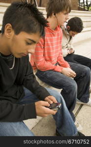 Teenage boy using a mobile phone with two other teenage boys sitting beside him