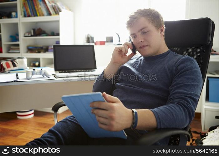 Teenage Boy Using Digital Tablet And Mobile Phone In Bedroom