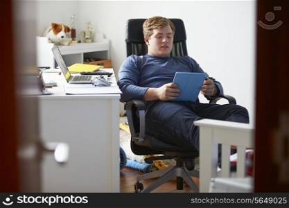 Teenage Boy Using Digital Tablet In Bedroom