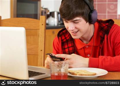 Teenage Boy Using Laptop And Listening To MP3 Player Whilst Eating Breakfast