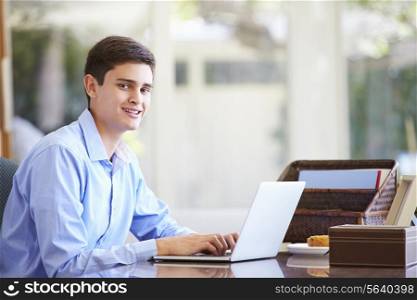 Teenage Boy Using Laptop On Desk At Home