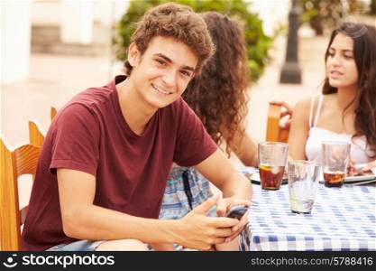 Teenage Boy Using Mobile Phone Sitting At Caf? With Friends