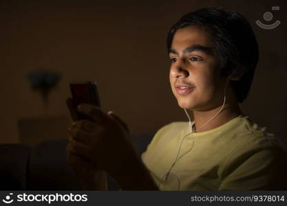 Teenage boy watching movie on smartphone at night in living room