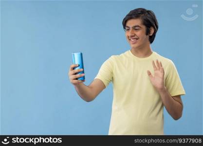 Teenage boy waving hand during video call on Smartphone against blue background