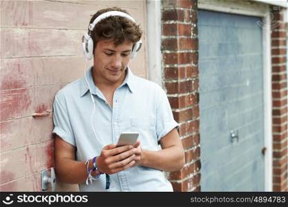 Teenage Boy Wearing Headphones And Listening To Music In Urban Setting