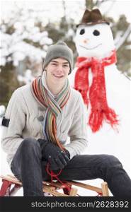 Teenage Boy With Sledge Next To Snowman