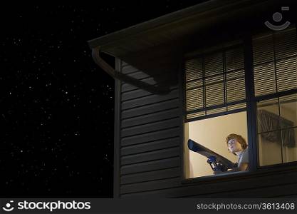 Teenage boy with telescope at open window looking at night sky