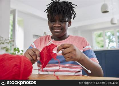 Teenage Boy With Wool Knitting On Table At Home