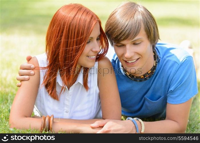 Teenage boyfriend and girlfriend holding hands lying on grass sunny