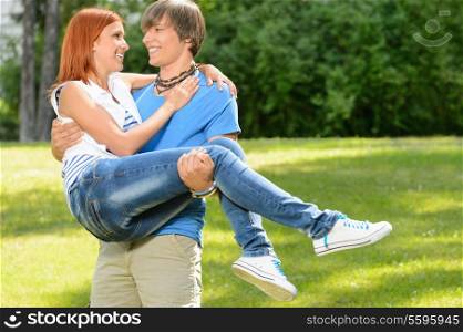 Teenage boyfriend carry girlfriend in his arms smiling in sunny park