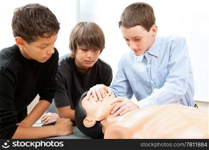 Teenage boys learn CPR life saving techniques on a mannequin.