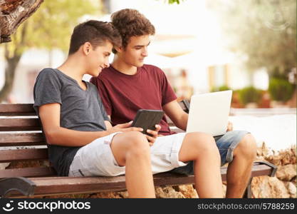 Teenage Boys On Park Bench Using Laptop And Digital Tablet