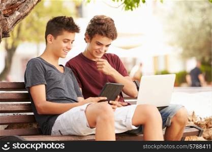 Teenage Boys On Park Bench Using Laptop And Digital Tablet