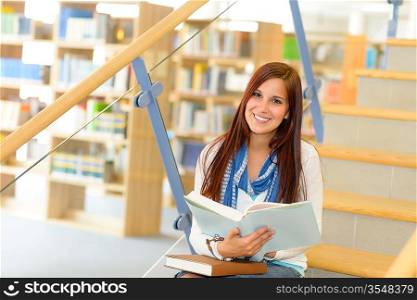 Teenage brunette student on high school library stairs reading book