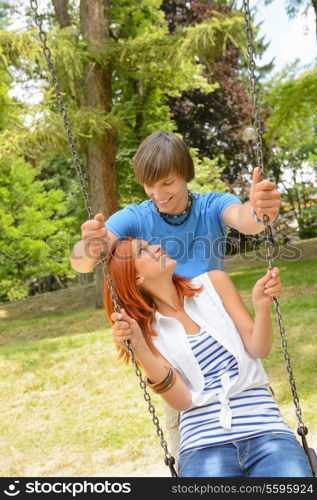 Teenage couple girl sitting on swing in park sunny day