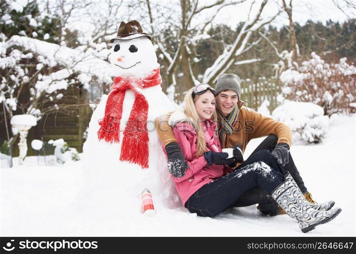 Teenage Couple In Winter Landscape Next To Snowman With Flask And Hot Drink