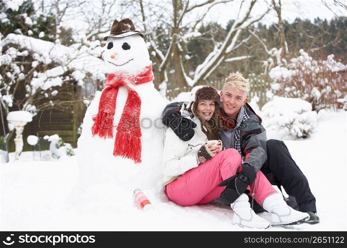 Teenage Couple In Winter Landscape Next To Snowman With Flask And Hot Drink
