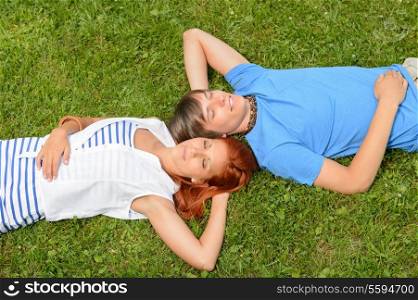 Teenage couple lying on grass relaxing closed eyes top view