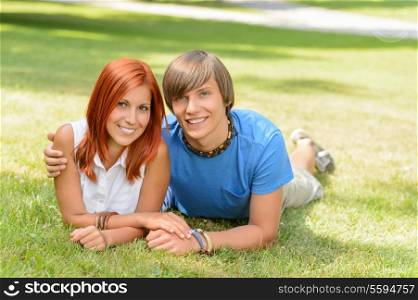Teenage couple lying on grass summer love smiling at camera
