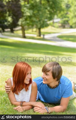 Teenage couple lying sunny park grass looking at each other