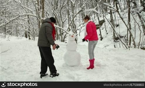 Teenage couple making a snowman in winter snowy forest