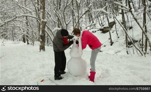 Teenage couple making a snowman in winter snowy forest