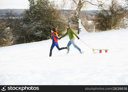 Teenage Couple Pulling Sledge Across Snowy Field