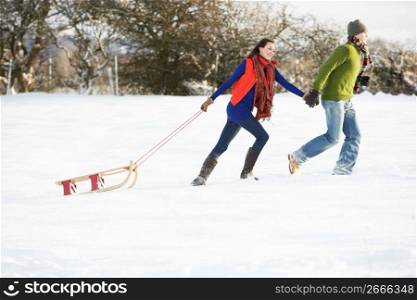 Teenage Couple Pulling Sledge Across Snowy Field