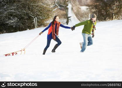 Teenage Couple Pulling Sledge Across Snowy Field