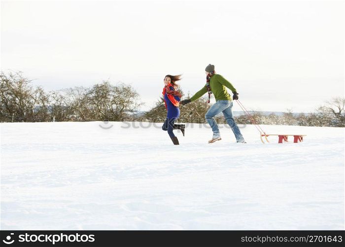Teenage Couple Pulling Sledge Across Snowy Field