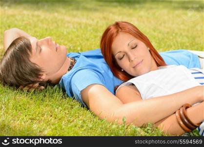 Teenage couple relaxing lying on grass closed eyes summer day