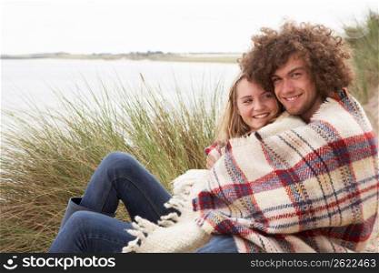 Teenage Couple Sitting In Sand Dunes Wrapped In Blanket