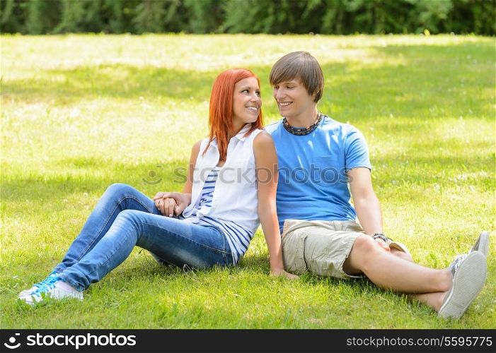 Teenage couple sitting on grass looking at each other summer