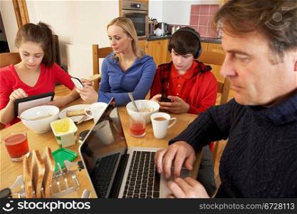 Teenage Family Using Gadgets Whilst Eating Breakfast Together In Kitchen