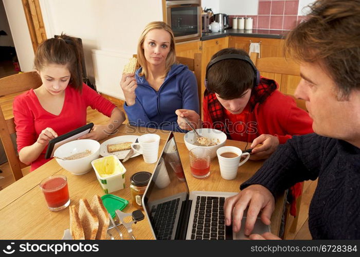 Teenage Family Using Gadgets Whilst Eating Breakfast Together In Kitchen