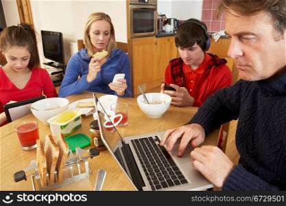 Teenage Family Using Gadgets Whilst Eating Breakfast Together In Kitchen