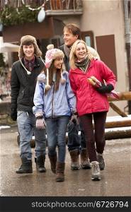 Teenage Family Walking Along Snowy Town Street In Ski Resort