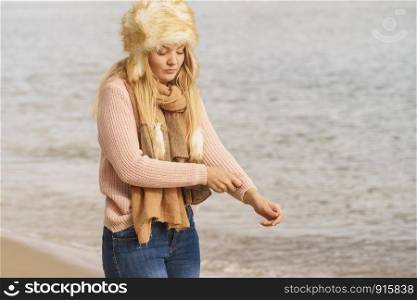 Teenage female spending time outdoor on the beach during autumn weather. Wearing sweater, scarf and fur hat.. Fashionable woman on beach