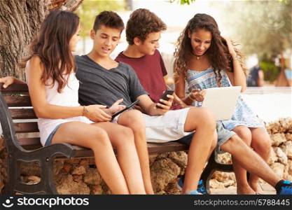 Teenage Friends Sitting In Park Using Digital Devices
