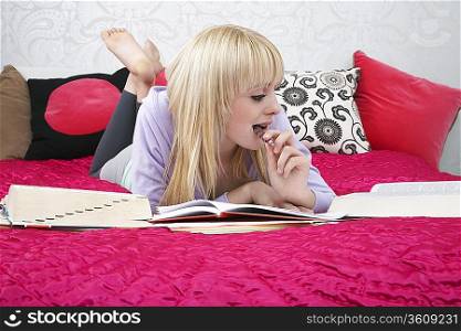 Teenage girl (16-17) lying on bed, doing homework