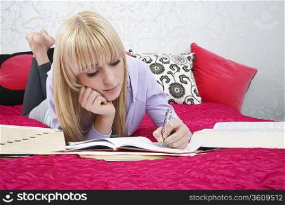 Teenage girl (16-17) lying on bed, writing