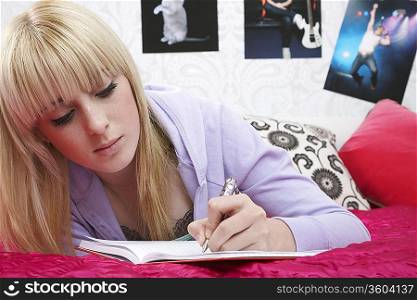 Teenage girl (16-17) lying on bed, writing diary