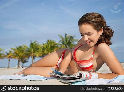 Teenage girl (16-17) reading magazine lying on beach