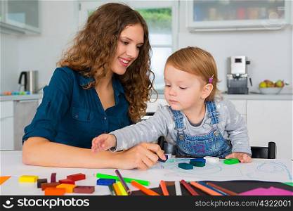 Teenage girl and female toddler drawing at kitchen table