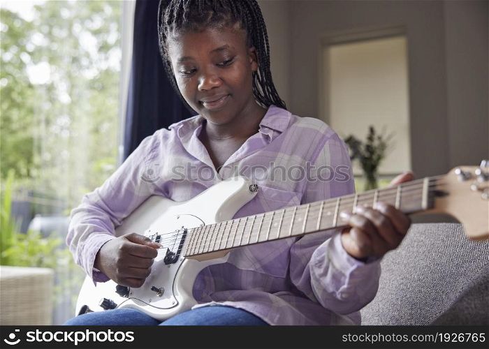 Teenage Girl At Home Learning To Play Electric Guitar