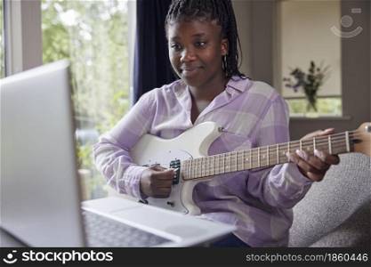 Teenage Girl At Home Learning To Play Electric Guitar With Online Lesson On Laptop Computer