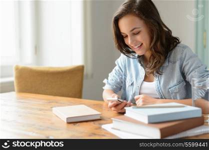 Teenage girl at home looking mobile phone smiling studying books