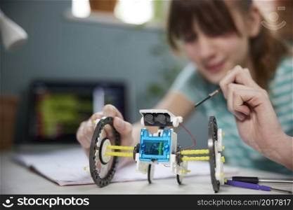 Teenage Girl Building Solar Powered Robot In Bedroom At Home
