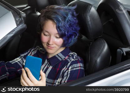 Teenage girl, cell phone in hand, looking at text while in driver seat of car. Focus on her face. Mixed Asian and Caucasian girl.