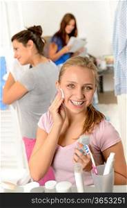 Teenage girl cleaning face with cotton pad with her friends